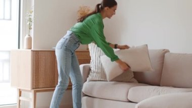 Home design. Young professional woman interior designer putting and correcting cushions on sofa, making it pretty and go away, tracking shot, slow motion, free space
