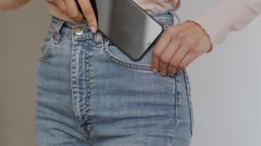 Close up shot of unrecognizable slim woman putting her modern smartphone into jeans pocket, slow motion, free space