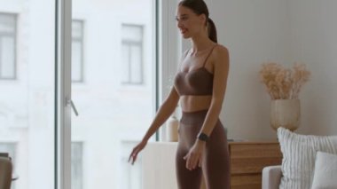 Bottocks workout. Young happy lady practicing squats exercise at home and rest after finishing it, training at home interior, tracking shot, slow motion, empty space