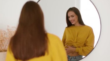 Love my body. Over shoulder portrait of young fit woman looking at herself at mirror and smiling, feeling satisfied of her sporty figure, tracking shot, slow motion, free space