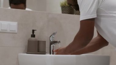 Morning hygiene. Close up shot of young african american guy washing his face in bathroom, looking at mirror, tracking shot, slow motion