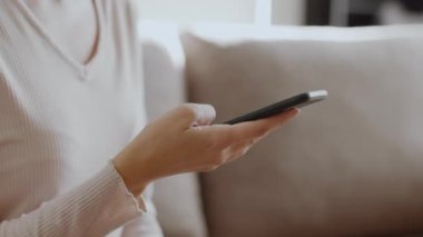 Life online. Close up shot of young unrecognizable woman web surfing on smartphone, scrolling social media, resting on sofa at home, tracking shot, slow motion, empty space