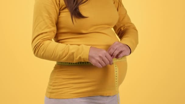 健康的な妊娠開発 閉じるアップショットの認識できない妊娠中の女性測定彼女のウエストとともにテープ 愛撫成長腹 オレンジスタジオの背景 スローモーション — ストック動画