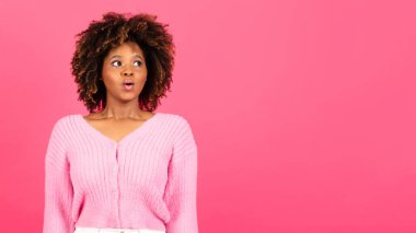 Surprised millennial african american curly lady in casual with open mouth looking at copy space, isolated on pink background, studio. Shock, ad and offer, fashion, beauty, lifestyle and emotions