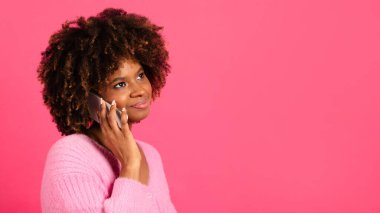 Happy pensive millennial african american curly woman in casual call by phone, look at copy space isolated on pink background, studio, close up. Communication, conversation, gossip, news, ad and offer