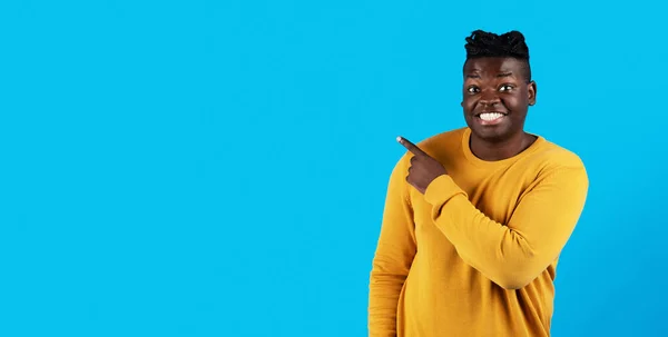 Joyful young black man pointing aside at copy space on blue background with finger, happy millennial african american guy demonstrating free place for your advertisement or design, panorama