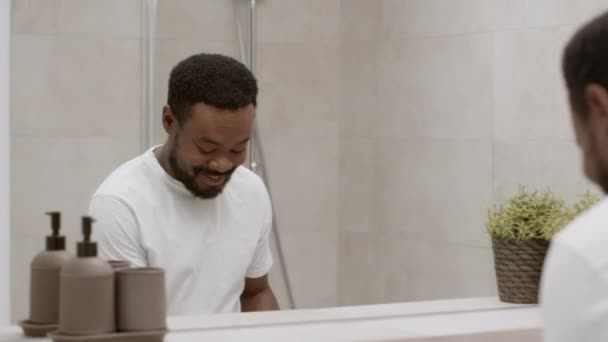 朝のやる気 若いですハンサムなアフリカ系アメリカ人男性洗顔顔でバスルームと笑顔に彼の反射 追跡ショット スローモーション 空のスペース — ストック動画