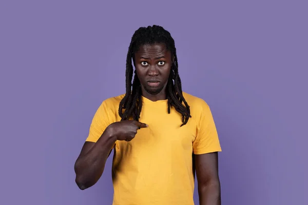 Are you talking about me. Surprised handsome millennial african american man with long dreadlocks, pointing at himself with confused face expression, posing over purple background