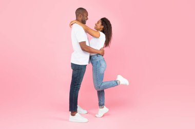 Side view of loving african american couple hugging and looking at each other on pink studio background, copy space. Black spouses having romantic moment together