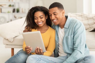 Technology for new normal at home. Glad millennial african american man and lady hug looking at digital tablet webcam in living room interior. Video call, meeting remote, chat and new app, covid-19