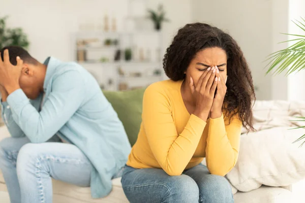 Sad crying young african american woman ignores offended man after quarrel, sit on sofa, think about breakup in home interior. Scandal, relationship problems, bad news reaction and crisis, divorce