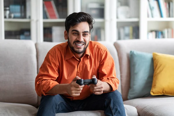自宅で休憩 国内エンターテイメント 自宅のソファの上に一人で座っている間 ハンサムな若い中東の男性がビデオゲームをして笑っています 現代のテクノロジーとエンターテイメント — ストック写真