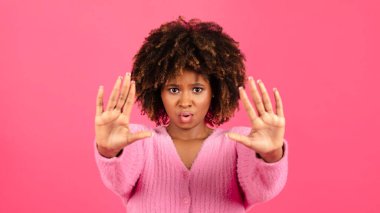 Angry sad confident millennial african american curly lady in casual show hands stop sign isolated on pink background, studio. Personal space, rejection, protection, fight with harassment and racism