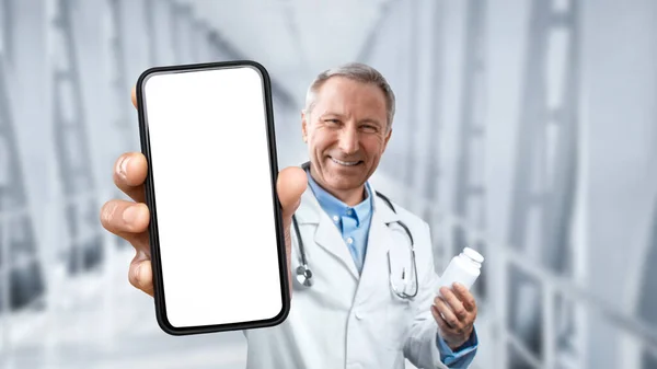 Online Medicine. Mature Male Doctor Holding Pills Jar And Showing Blank Smartphone At Camera While Standing In Clinic Hall, Therapist Man Recommending Modern Mobile App Or Website, Collage, Mockup