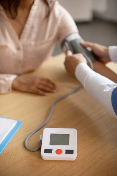 Middle aged korean doctor measures blood pressure with tonometer of young black female patient in clinic office interior. Health care, treatment of high pressure, visit to therapist and medical exam