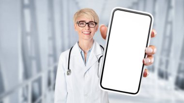 Smiling Doctor Lady In Uniform Showing Big Smartphone With Blank Screen At Camera While Standing In Hospital Hall, Cheerful Female Physician Recommending Mobile App For Telemedicine, Collage, Mockup