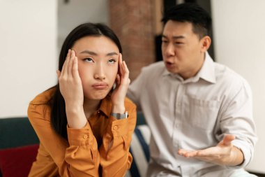 Emotional japanese mature man gesturing and shouting at his wife, chinese couple having quarrel at home. Domestic abuse, relationship crisis concept