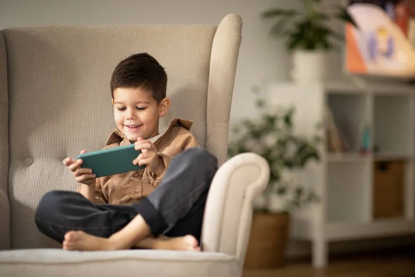 Cheerful Cute Little European Boy Sits Armchair Watches Video Smartphone —  Fotos de Stock