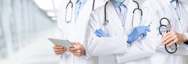 Group of unrecognizable male doctors posing at modern clinic, holding stethoscopes, digital tablet, syringe for injection, cropped shot, panorama, copy space for advert. Healthcare, hospital, medical
