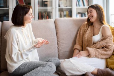Laughing pretty european millennial female listen friend in sweater, sit on sofa, enjoy meeting and spare time in comfort living room interior. Communicate together, relationships and gossip at home
