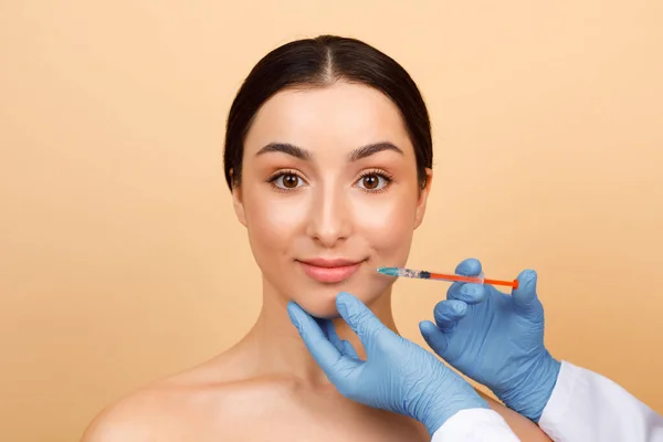 Injection Cosmetology. Beautician Doctor Making Lip Augmentation Procedure To Young Indian Woman, Beautiful Hindu Female Getting Hyaluronic Acid Shot While Standing Over Beige Background, Copy Space