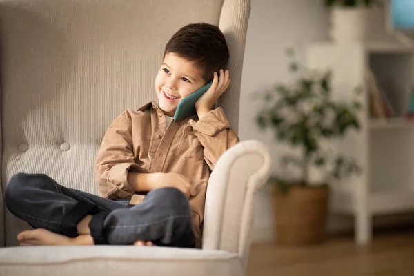 Cheerful Cute Small Boy Sits Armchair Calls Smartphone Talk Cozy — Stock fotografie