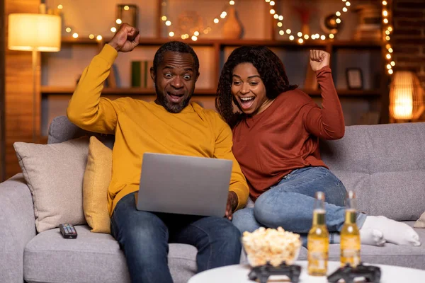 宝くじ プレゼント 感情的に幸せな美しいアフリカ系アメリカ人カップルギャンブルでインターネット上の自宅で 陽気な黒人男性と女性の勝者は ソファに座って ラップトップを使用して 立ち上がり拳 — ストック写真