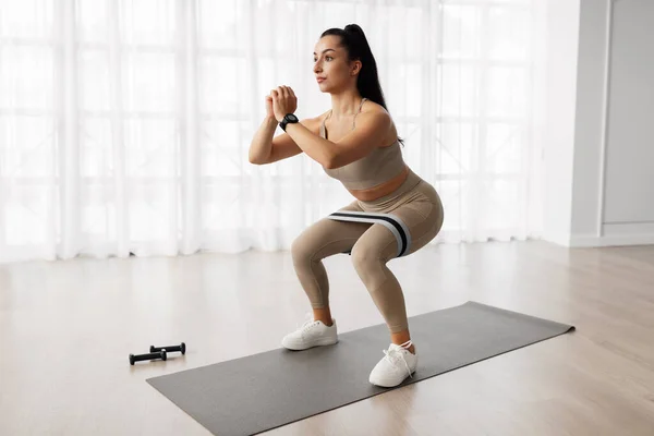 Motivated athletic beautiful young hispanic woman in sportswear standing on yoga mat, doing workout at home, using fitness tools, looking at copy space, full length candid shot