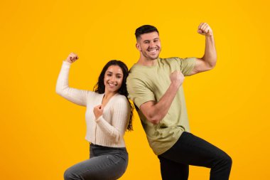 Cheerful excited young arabic couple in casual make gesture of success and victory, rejoice together, isolated on yellow background, studio. Reaction to win, good news, surprise, sale, ad and offer