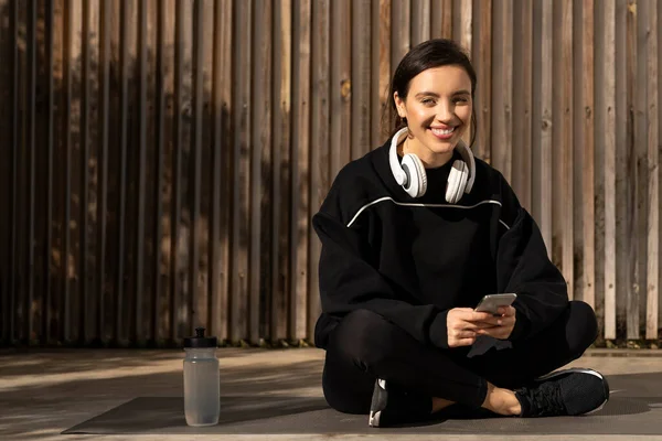 Happy Young European Woman Athlete Sportswear Headphones Sits Floor Smartphone — Zdjęcie stockowe