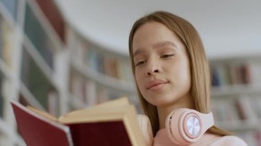 Close up portrait of young interested woman student reading book at library, looking for important information, turning pages, below view, tracking shot