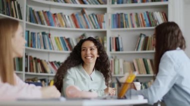 College friendship. Group of young carefree women students laughing at library interior, studying and discussing educational project together, tracking shot, slow motion, free space