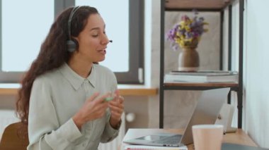 Telemarketing concept. Young professional woman sales agent in headset with mic video chatting with client online via laptop, working from office, empty space