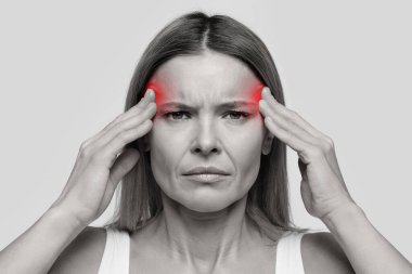 Unhappy stressed middle aged woman with headache touching inflamed zones her temples, isolated on studio background, emotional black and white closeup photo
