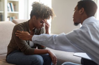 Black man in formal outfit psychologist comforting touching shoulder upset frustrated woman patient, unhappy african american woman have therapy session, suffering from depression