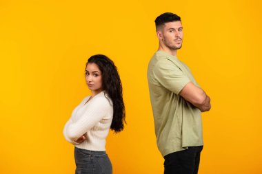 Sad offended young middle eastern woman ignores boyfriend in casual with crossed arms, think about divorce isolated on yellow background, studio. Relationship problems, quarrel, emotions and breakup
