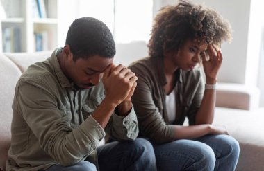 Upset african millennial man and woman in casual sitting on couch at clinic, feeling down after quarrel, black spouses having fight, experiencing difficulties in marriage, attending therapy session