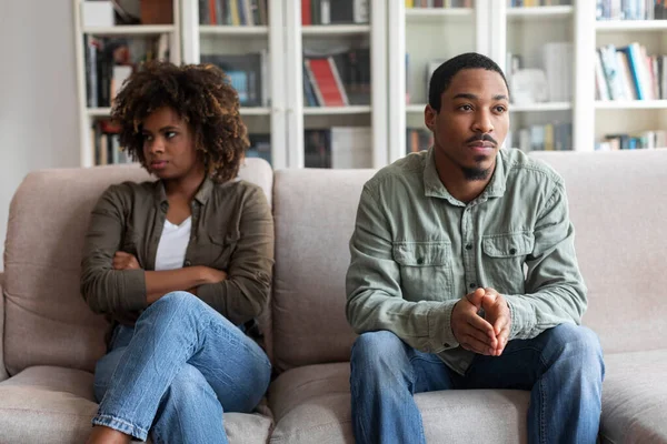 Sad unhappy young black man and woman in casual sitting on couch at home, feeling down after quarrel, african american spouses having fight, experiencing difficulties in marriage, relationships
