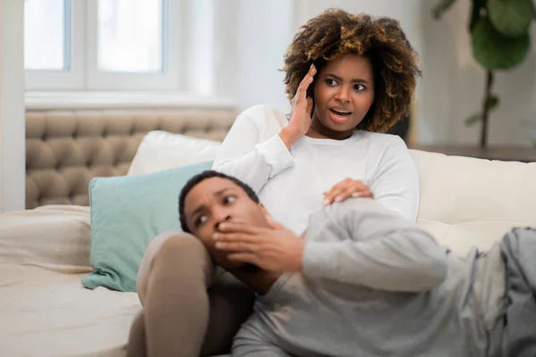 Shocked frightened millennial black couple man and woman in homewear sitting, lying on couch. watching horror movie together at home, copy space