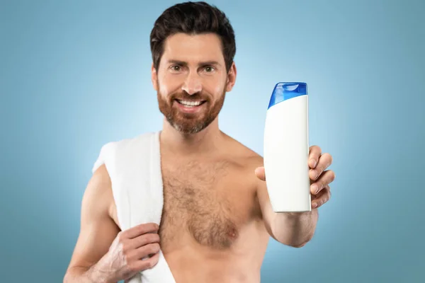 Happy Handsome Man Showing Shampoo Bottle Standing Towel Blue Background — Stockfoto