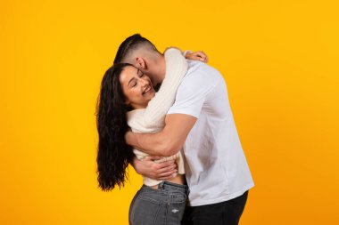 Satisfied young arabic husband hugging wife, enjoy tender moment, time together, have fun, look at camera, isolated on yellow background, studio. Date, family relationship, couple love, ad and offer
