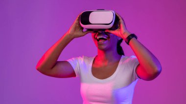 Modern Technologies For Entertainment. Portrait Of Excited Black Woman Wearing VR Headset In Neon Light, Happy Young African American Female Experiencing Virtual Reality While Playing Video Game