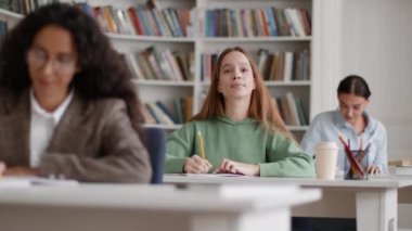 Incomprehensible topic. Tracking shot of group of female students studying at classroom, one lady raising hand and asking question, slow motion, selective focus, free space
