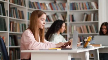 Great modern education. Young pretty smart woman student typing on laptop, turning face to camera and gesturing thumb up, studying at campus library, tracking shot, slow motion, empty space