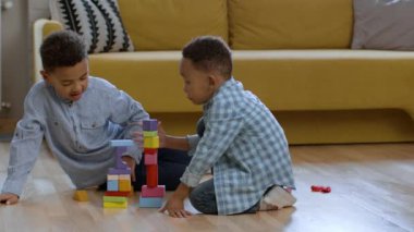 Brotherhood and friendship. Cute happy african american brothers playing together at home, building towers with wooden blocks and laughing, tracking shot, slow motion, empty space