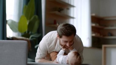 Fatherhood and babysitting. Young happy dad playing with his newborn baby daughter, blowing at her, carefree girl laughing, slow motion, empty space