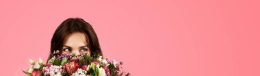Smiling young caucasian lady enjoy aroma of bouquet of flowers, rejoices at gift, isolated on pink background, panorama, studio. Celebration of birthday, holiday in spring, lifestyle, ad and offer