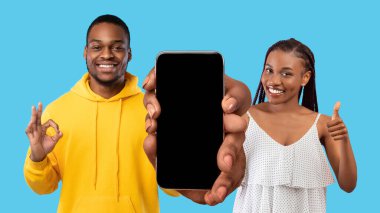 Great Offer. Young African American Couple Demonstrating Big Blank Smartphone At Camera And Showing Thumb Up And Ok Gestures, Black Man And Woman Recommending New App Or Website, Mockup