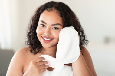 Portrait of happy oversize lady drying clean face with soft white towel after morning washing, smiling at camera. Facial hygiene and skincare concept