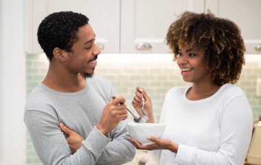 Loving african american young couple have breakfast together at home, handsome man and curly woman eating granola or oatmeal together, lovers having conversation. Family, marriage, relationships